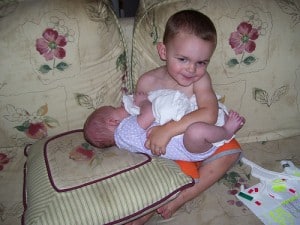 A toddler holds his newborn baby brother.